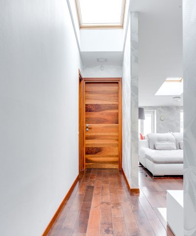 Minimalist corridor with wooden flooring and skylight, leading to a modern living area.